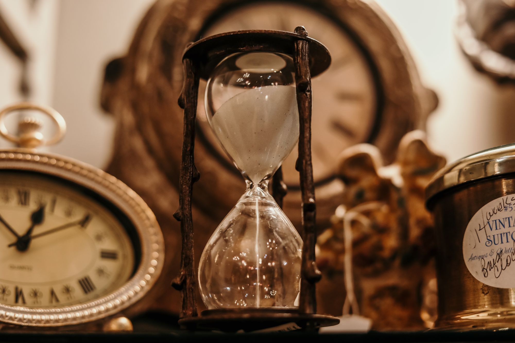 An hourglass with sand running through it, beside vintage clocks