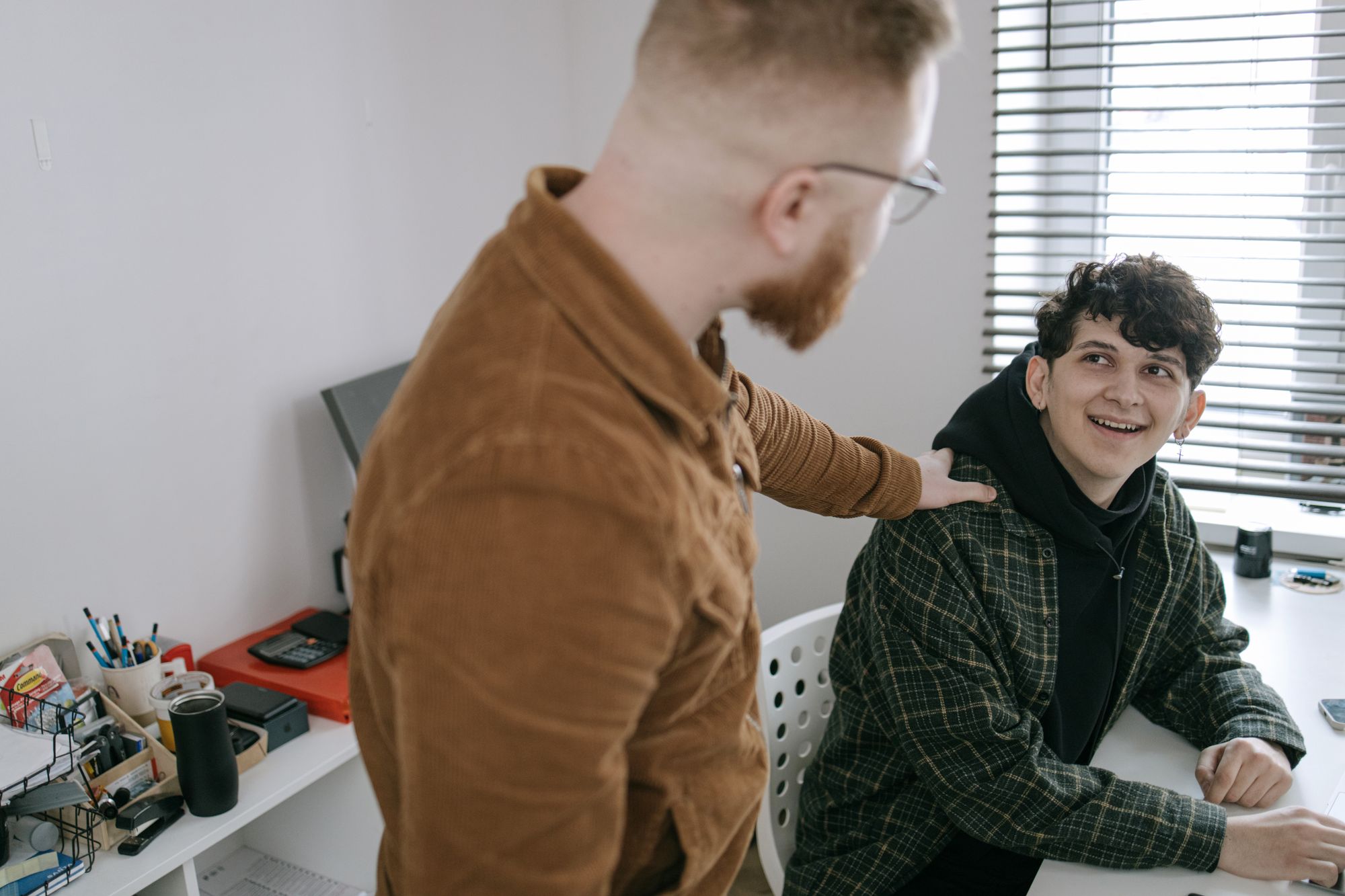 A colleague resting a supportive hand on a co-worker's shoulder at a desk