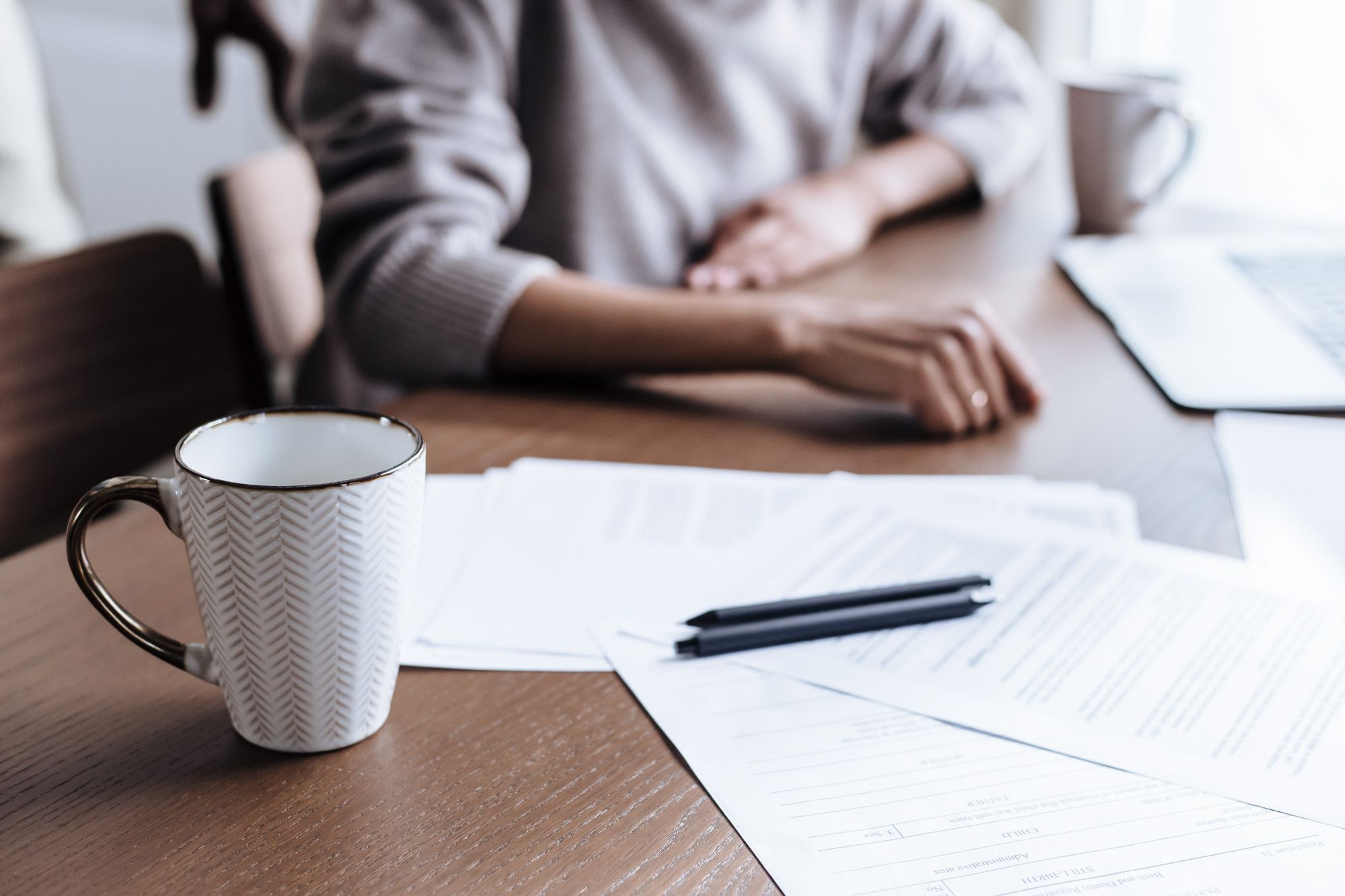 Documents, a pen and a mug on a wooden table in natural light