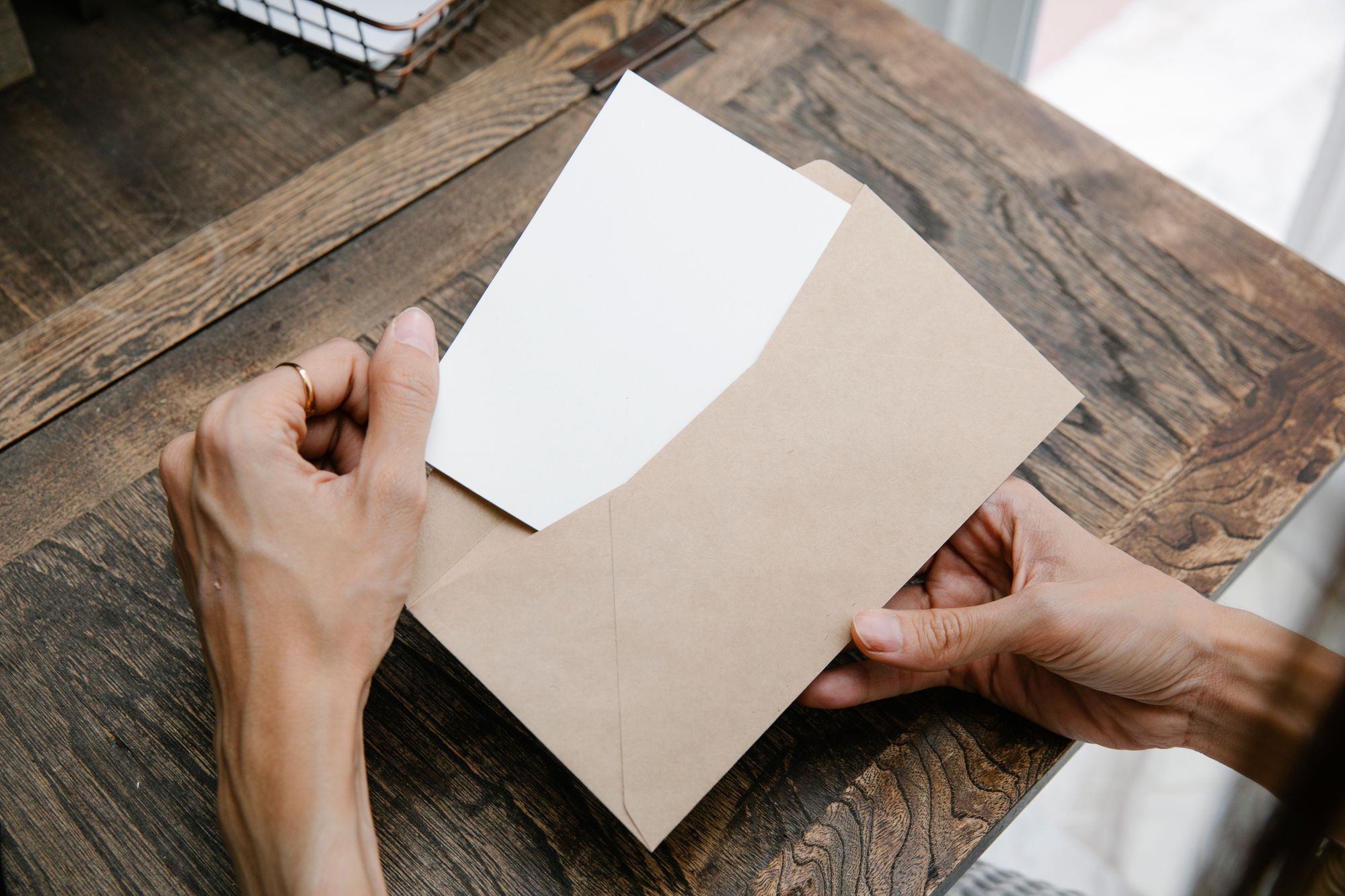 A person opening a letter from a brown envelope at a wooden table